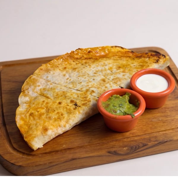 Golden-brown quesadilla triangles with guacamole and sour cream on a wooden board.