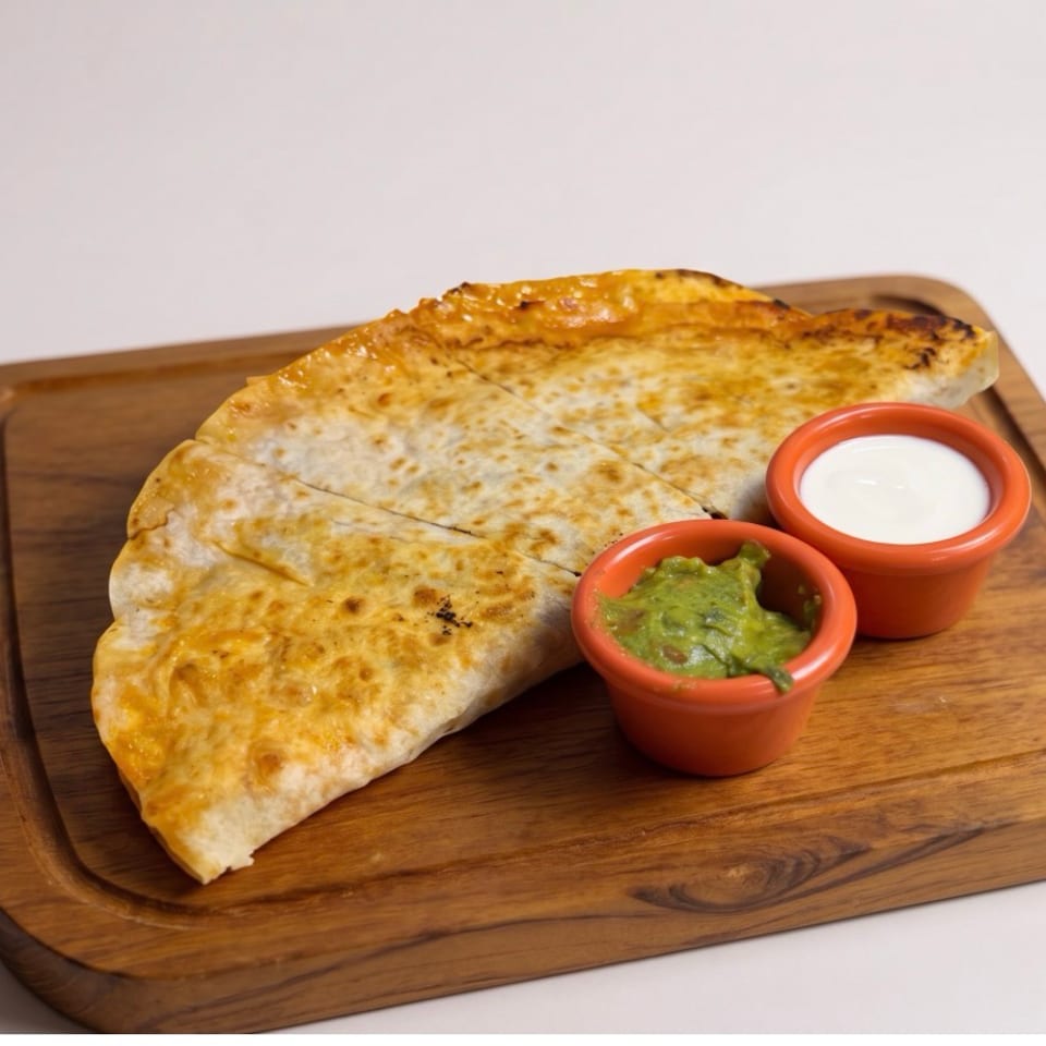 Golden-brown quesadilla triangles with guacamole and sour cream on a wooden board.