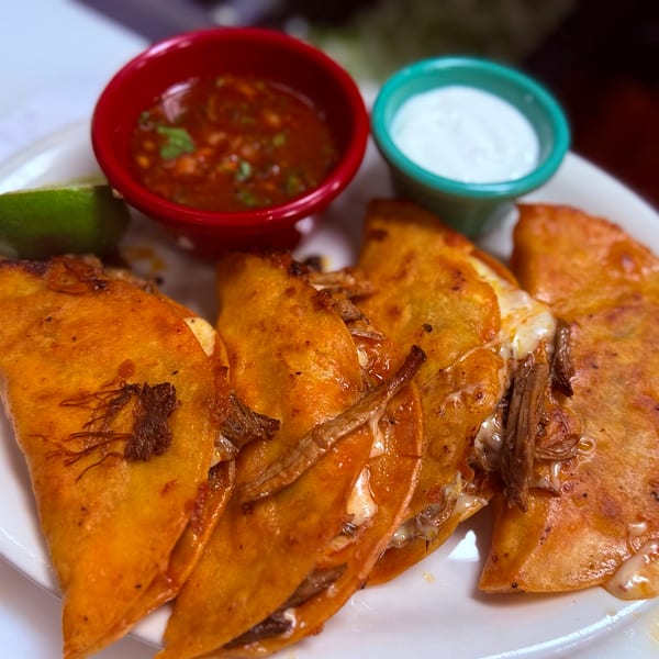 A plate of five golden-brown birria tacos with melted cheese, served with lime, salsa, and sour cream.