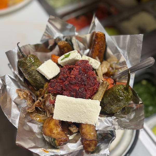 A foil-lined bowl filled with red meat, white cheese, green peppers, and plantains.