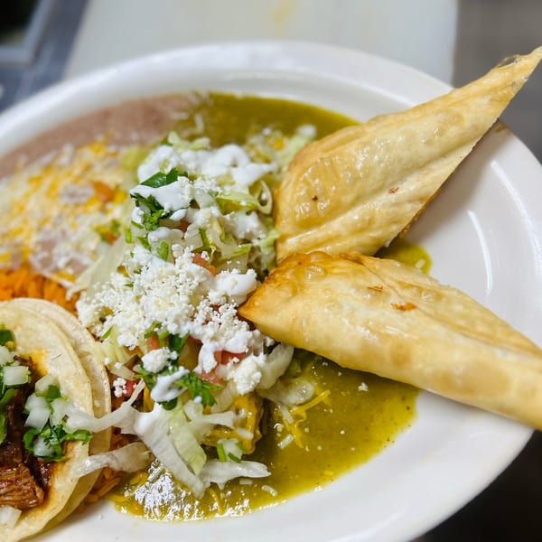 A plate of Mexican food with two tacos, rice, refried beans, and two fried pastries.